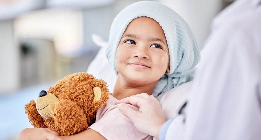 A smiling young girl in a head scarf hugging a teddy bear
