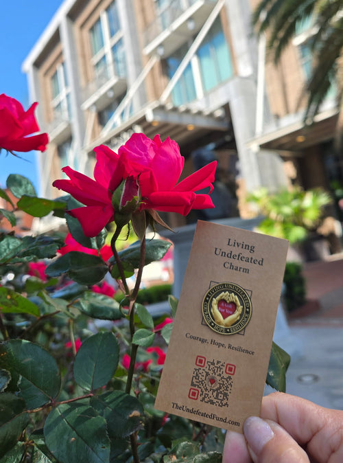A Living Undefeated Charm held up beside red roses outside a building