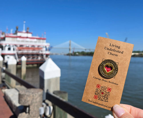 A Living Undefeated Charm held up by the water with a riverboat and bridge behind it