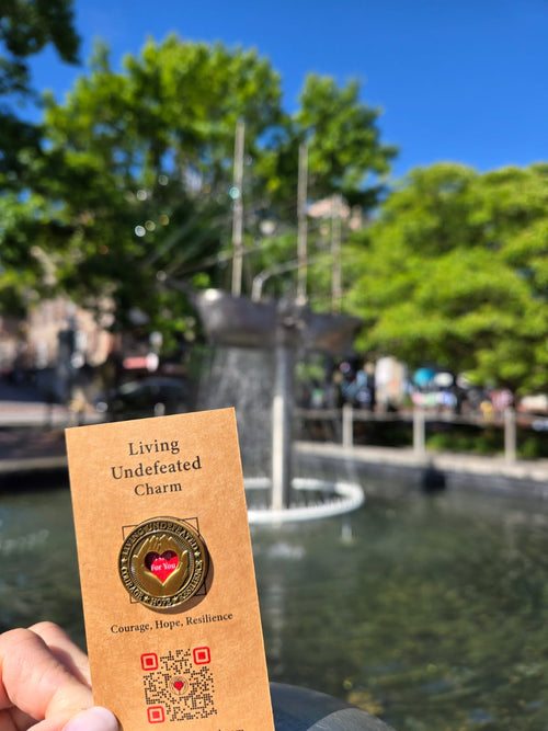 A Living Undefeated Charm held up beside a fountain in a city park
